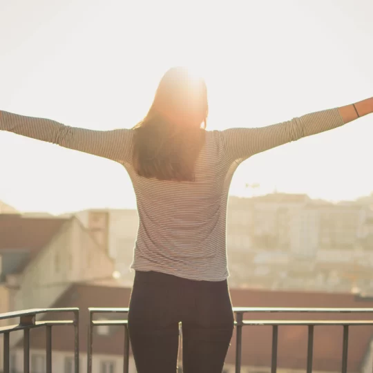 Une femme les bras écartés face au soleil